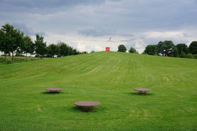 Scenic view of golf course against cloudy sky