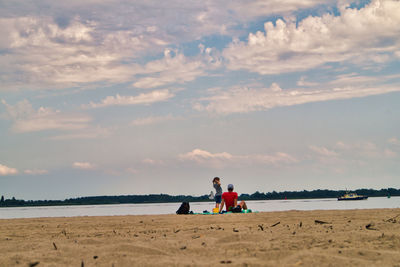 Men sitting on beach against sky