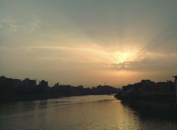 Silhouette city by river against sky during sunset