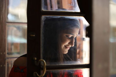 Smiling young woman looking down seen through glass window