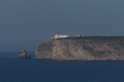 Lighthouse by sea against clear sky