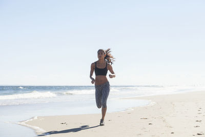 Confident woman jogging on shore at beach against sky