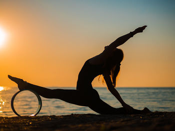 Silhouette woman doing yoga at beach against sky