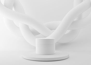 White and blank, unbranded cosmetic cream jar standing on podium with abstract white splines.