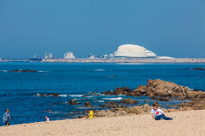 Rear view of people on beach against clear blue sky