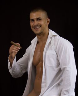 Muscular man with cigar standing against black background