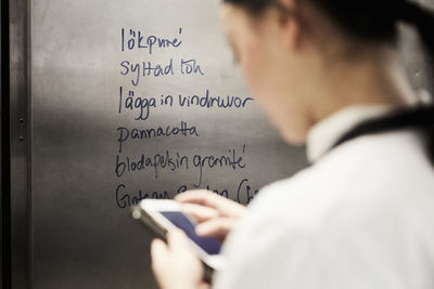 Rear view of female chef using mobile phone with text on metal in commercial kitchen