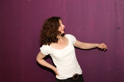 Smiling beautiful woman looking away against purple wall at garage