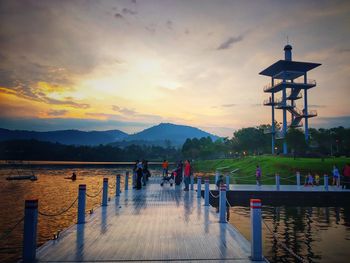 People on lake against sky during sunset