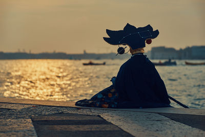 Rear view of carnival mask looking at sea against sky