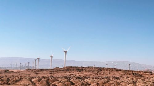 Wind turbines on land against clear sky