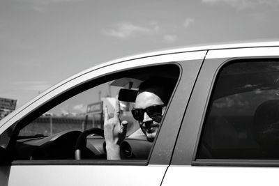 Portrait of mid adult man gesturing horn sign while driving car during sunny day
