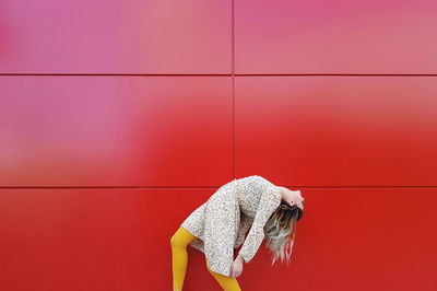 Side view of young woman bending by red wall