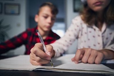 Midsection of girl writing in book siting at home