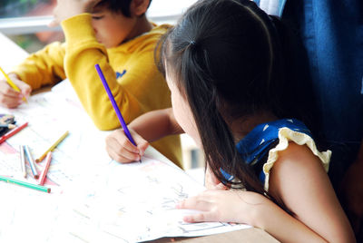 Teacher standing by children drawing on paper