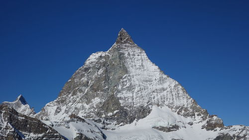 Low angle view of snowcapped mountain against clear blue sky