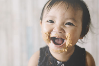 Close-up portrait of cute girl with peanut butter on face at home