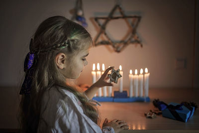 Cute girl holding star shape while standing against burning candles