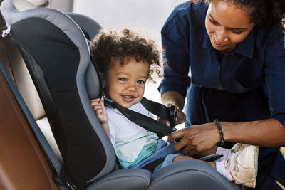 Portrait of smiling boy while mother tying seat belt