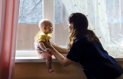 Young mother holds her baby near the window