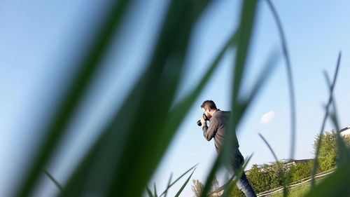 Rear view of man photographing through digital camera on field