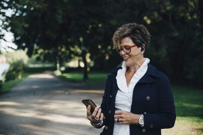 Senior woman wearing hands free device while using mobile phone in park