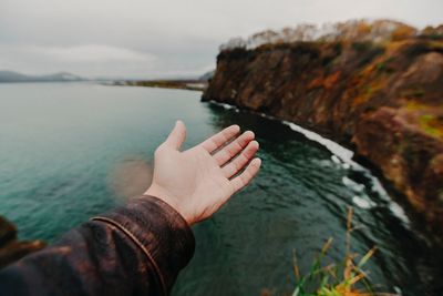 Cropped image of hand against sea at beach