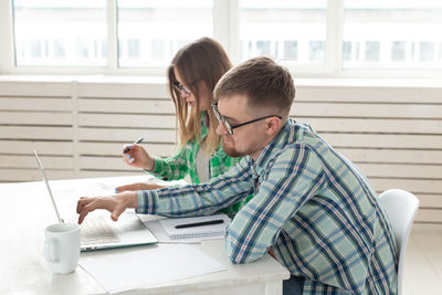 Man and woman using mobile phone while sitting on table