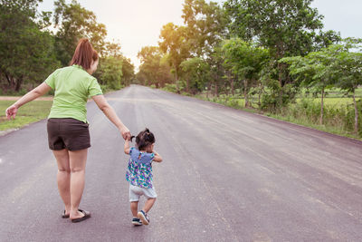 Rear view of woman with daughter walking on road amidst trees