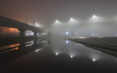 Illuminated bridge over river against sky at night