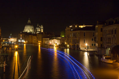 Illuminated city by river against sky at night