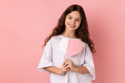 Portrait of young woman standing against pink background