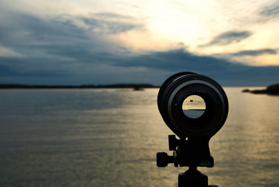 Coin-operated binoculars by sea against sky during sunset
