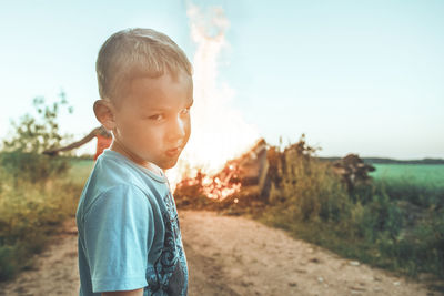 Portrait of boy standing on dirt road against sky