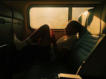 Side view of young man using mobile phone while sitting on seat in train