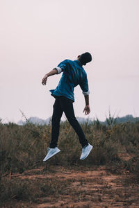 Full length of man jumping on field against clear sky