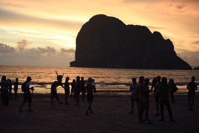 Group of people at beach against sky during sunset