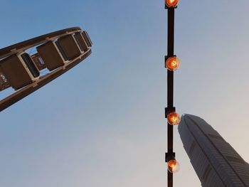 Low angle view of illuminated bulbs amidst ferris wheel and building against sky