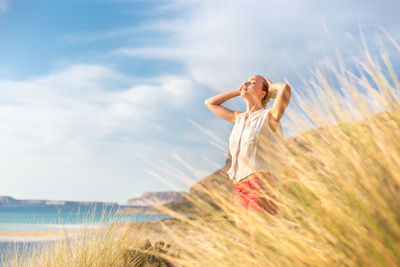 Woman with arms raised on field against sky