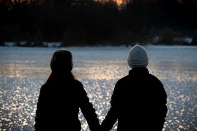 Rear view of silhouette friends standing against snow during winter