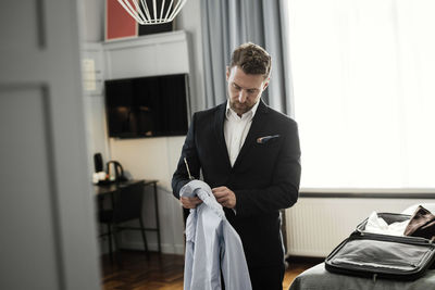 Mature man holding shirt in coathanger standing at hotel room