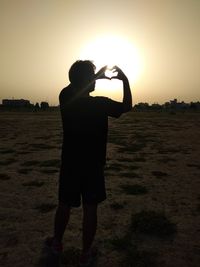 Rear view of silhouette man photographing on field against sunset sky