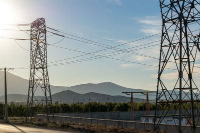 Electricity pylons by mountains against sky during sunset