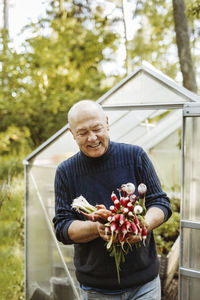 Happy gay man holding fresh root vegetables at garden