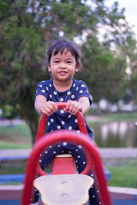 Portrait of cute girl sitting on seesaw at playground