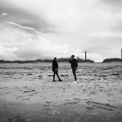 Rear view of men walking on field against sky