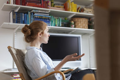 Side view of woman talking while sitting on chair at home