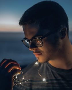 Close-up of young man holding illuminated string lights at night