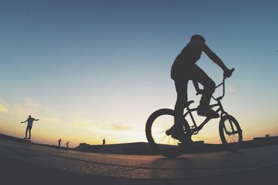 Low angle view of silhouette woman riding bicycle at sunset