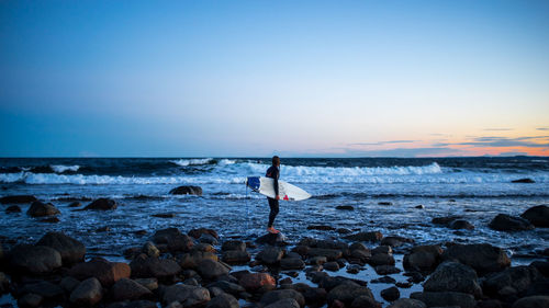 Side view of woman with surfboard standing at beach